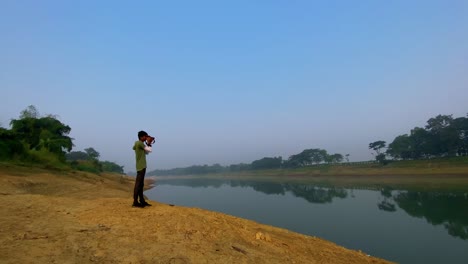 Junger-Mann-Mit-Lässiger-Kleidung,-Der-Fotos-Mit-Dslr-kamera-Im-Freien-Am-Fluss-Macht