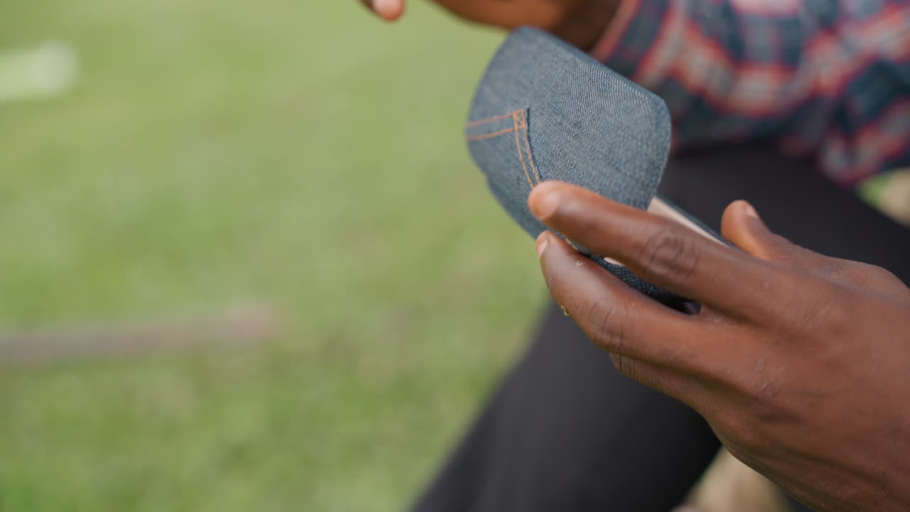 Closeup black father hands cleaning sunglasses with textured case on grass bench, slow careful polish with microfiber cloth, warm afternoon light, intimate bond and focused attention as father tends