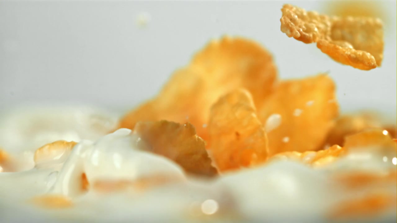 Goldene Cornflakes spritzen in Zeitlupe in frische Milch