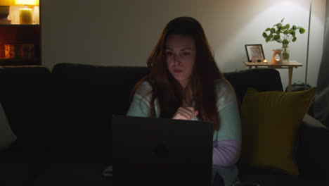 anxious woman sitting on sofa at home at night closing laptop concerned about social media or bad news