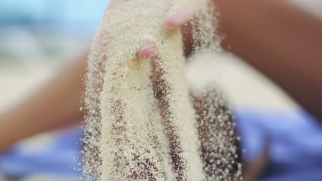 woman lifting up beach sand and letting it fall down in slow motion