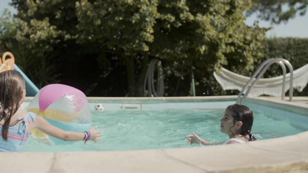 Bambini felici che giocano a palla in piscina in una giornata di sole.