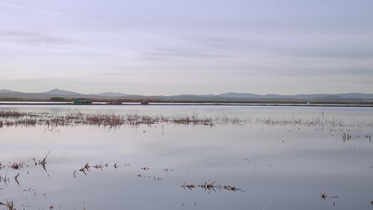 몇 대의 자동차가 지평선에서 천천히 움직이는 얕은 호수의 고요한 전망