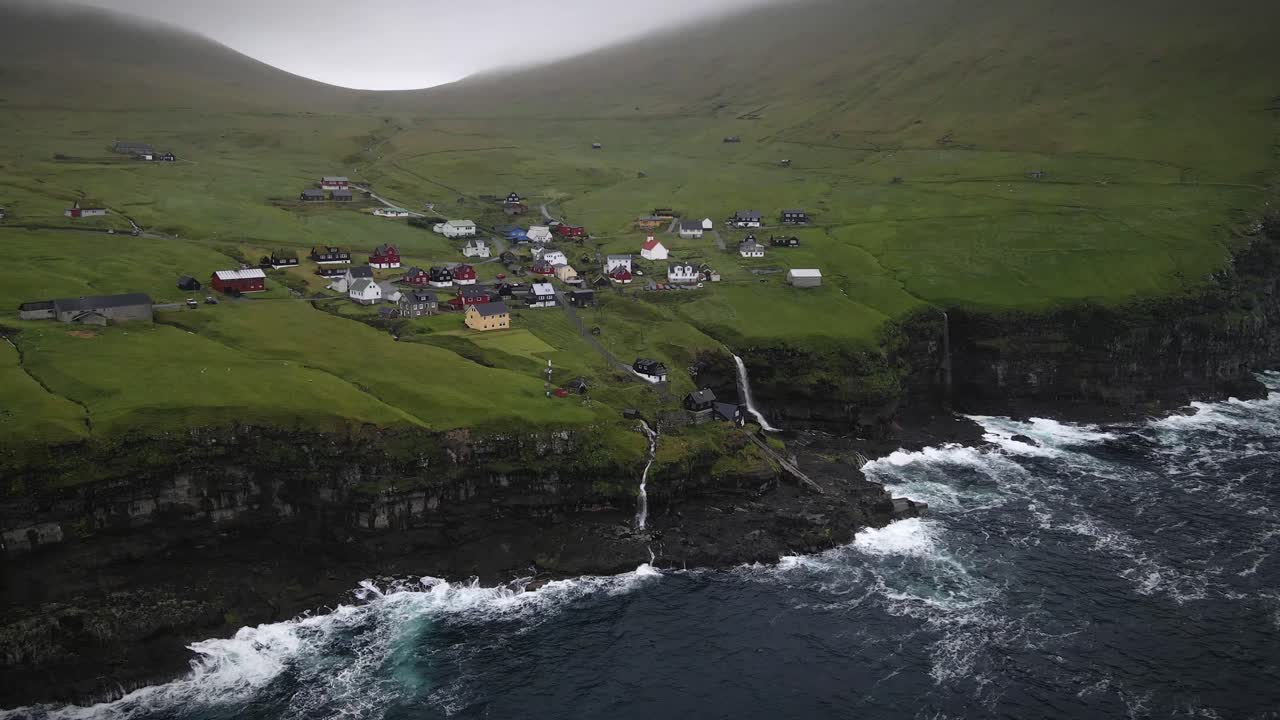vista aérea capturando el pintoresco pueblo de mikladalur en la isla de kalsoy, con una impresionante cascada en cascada en el océano en medio de dramáticos acantilados, islas feroe, drones en órbita