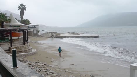 Distant-shot-of-person-running-away-from-sea-waves-in-slow-motion-on-a-rainy-cloudy-day