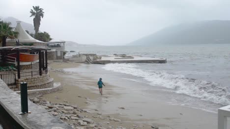 Toma-Distante-De-Una-Persona-Que-Huye-De-Las-Olas-Del-Mar-En-Cámara-Lenta-En-Un-Día-Lluvioso-Y-Nublado