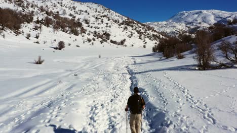 hombre con pantalones de senderismo de color caqui y polo negro hace caminatas nórdicas con sus botas de montaña en una gruesa capa de nieve en el monte hermon en israel en un día soleado