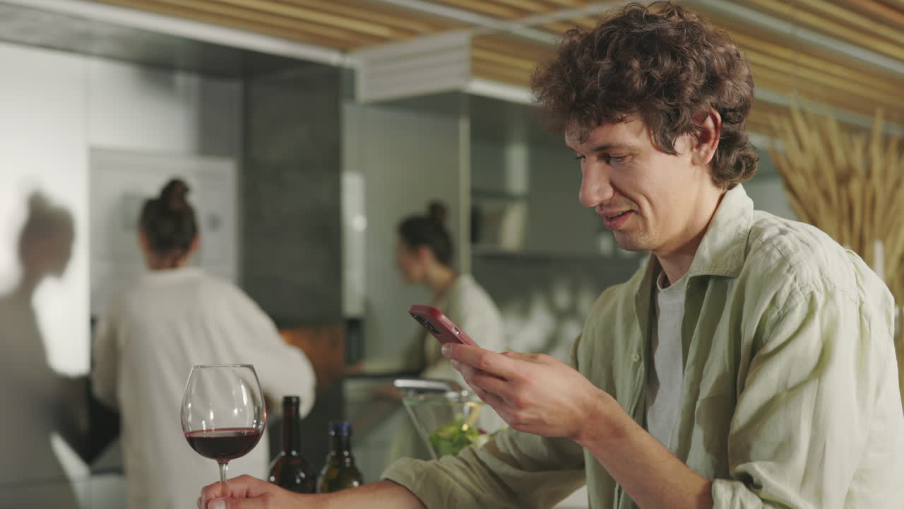 Man Using Smartphone in a Modern Kitchen with Friends