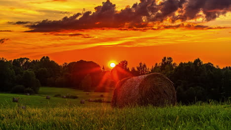 time lapse shot of farmland with hay bales and beautiful orange sunset at sky in backdrop - flying clouds during autumn day on countryside field