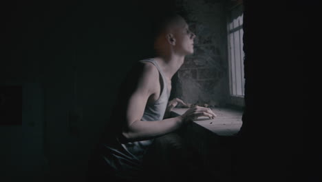 pale bald skinny man looks through the window in the creepy old bathroom at night