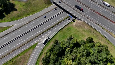Trucks and cars on new build Germany autobahn on sunny day in rural suburb. Aerial tilt up wide shot. Traffic Scene on modern freeway road. Multi-lane intersection in town