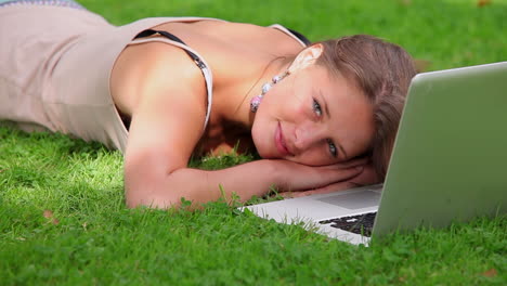 happy student lying on grass looking at laptop