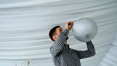 hombre colgando coloridas linternas de papel gris rosa blanco en el techo.