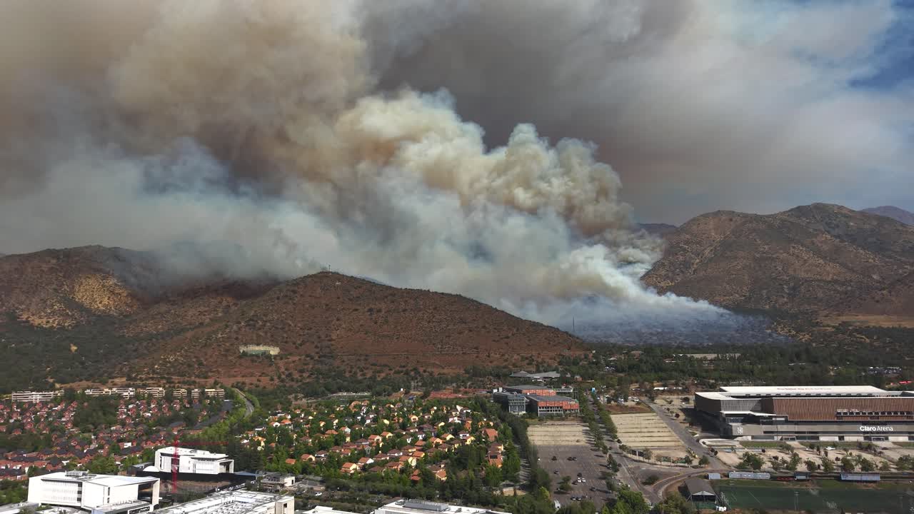 Prospettiva aerea da drone di un'enorme colonna di fumo di un incendio che incombe su un'area residenziale vicino alle montagne, che illustra un'emergenza ambientale e un disastro naturale in Cile e in 4K