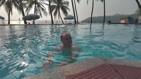 4k video of an older man swimming in a luxury resort swimming pool surrounded with palm trees in india
