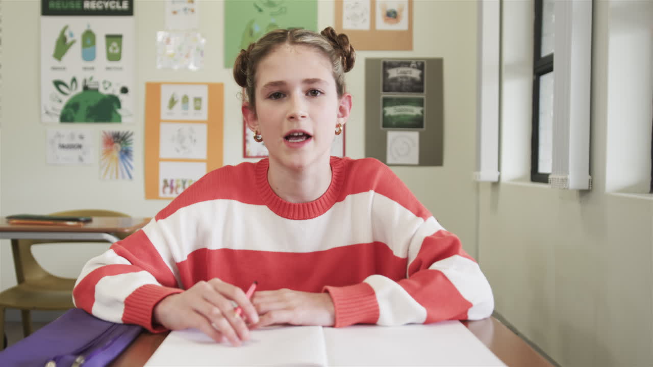 On video call, In school, young girl holding pencil focusing on writing assignment in classroom