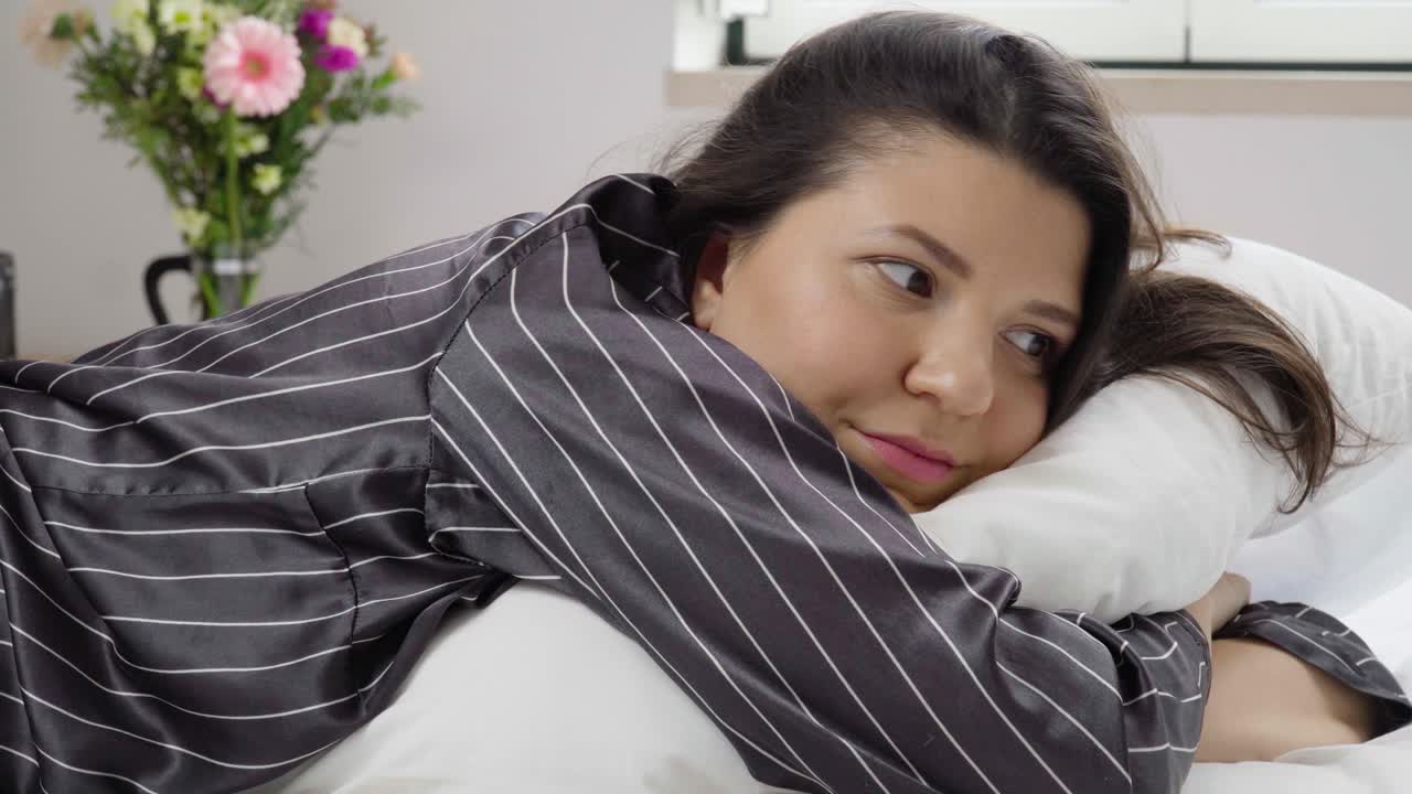 잠옷을 입은 젊은 꿈꾸는 여성이 침대에 누워 베개, 슬라이더를 포옹하고 있습니다.