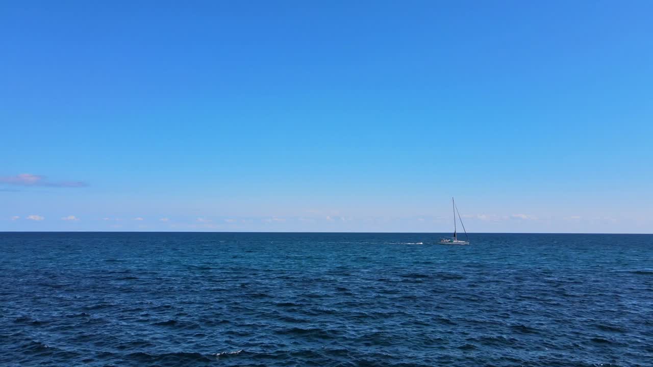 A serene sailboat navigates the crystal-clear waters off Cala Varques, showcasing the beauty of Porto Cristo. The bright blue sky enhances the peaceful atmosphere.