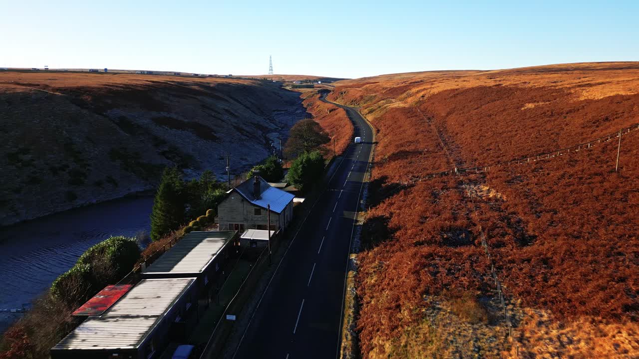 vista aérea en movimiento de los páramos pasando por una casa de campo en una calle tranquila en el páramo de saddleworth, mostrando un paisaje salvaje con tráfico, embalses y páramos bordeados de nieve