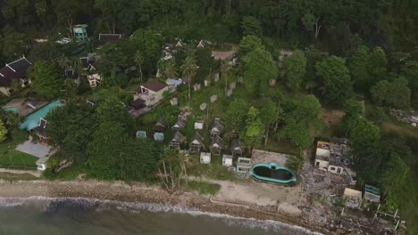 Aerial-birds-eye-view-of-a-beach-with-2-open-resorts-and-one-abandoned-and-derelict-beach-bungalow-tourist-resort-in-Koh-Chang-Thailand-due-to-the-effect-of-covid-on-global-travel-and-tourism