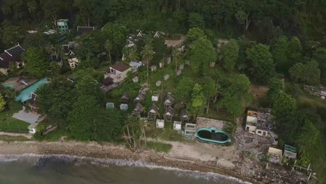 aerial birds eye view of a beach with 2 open resorts and one abandoned and derelict beach bungalow tourist resort in koh chang thailand due to the effect of covid on global travel and tourism