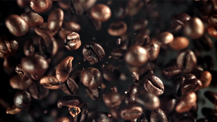 Grãos de café torrados caindo em câmera lenta com fumaça