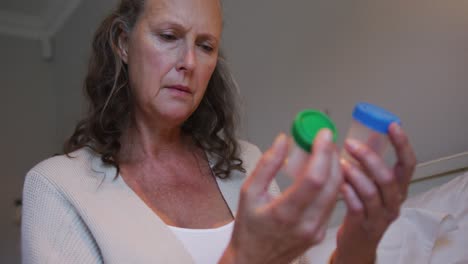 Confused-senior-caucasian-woman-holding-and-looking-at-two-bottles-of-tablets