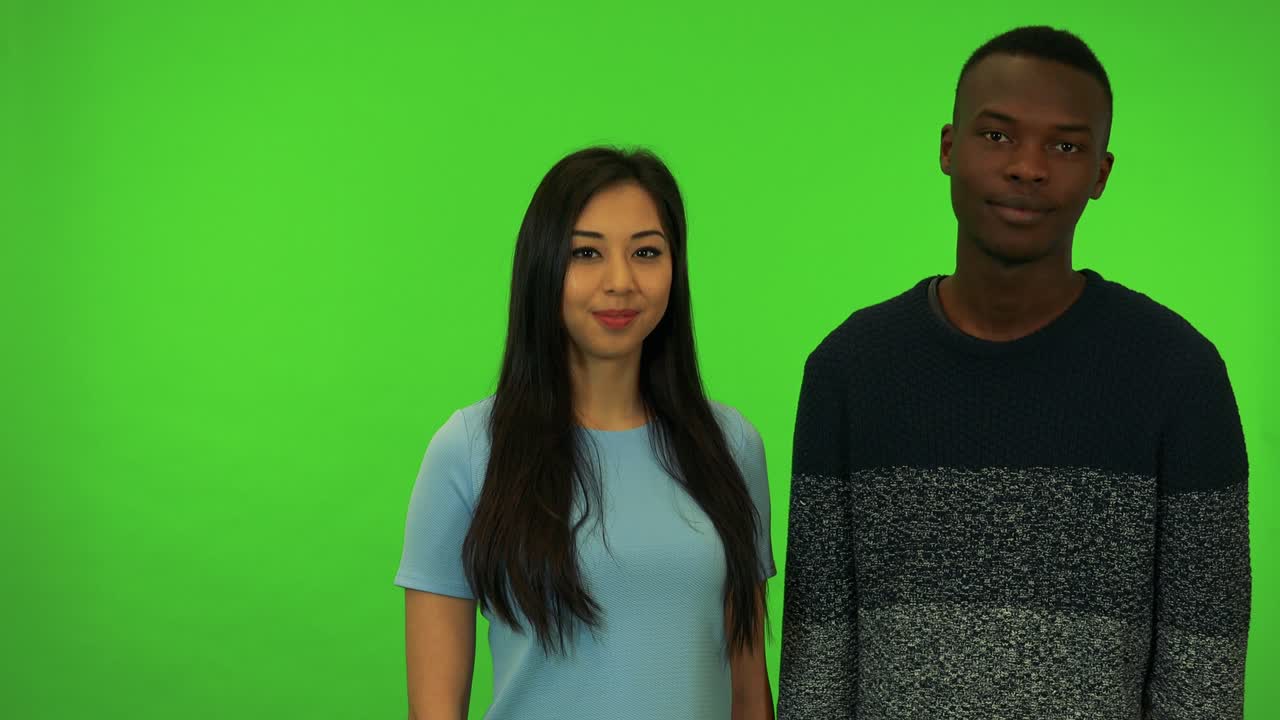 Uma jovem asiática e um jovem negro acenam com a cabeça para a câmera - estúdio de tela verde.