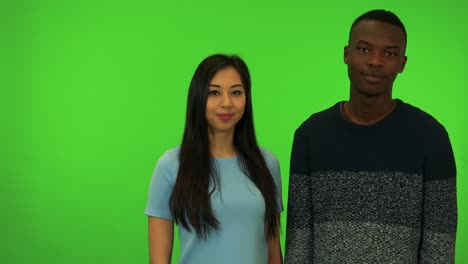 a young asian woman and a young black man nod at the camera - green screen studio