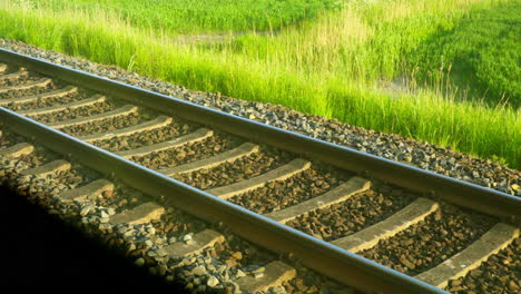 Vista-Cercana-De-Las-Vías-Del-Tren-Desde-La-Ventana-En-Un-Día-Soleado,-Hierba-Verde-En-La-Naturaleza