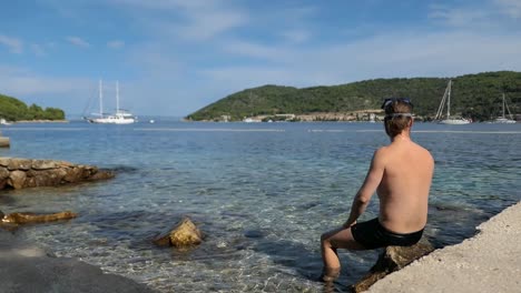 Hombre-Poniéndose-Una-Máscara-De-Snorkel-Y-Mirando-La-Vista-Al-Mar,-Isla-Vis,-Croacia