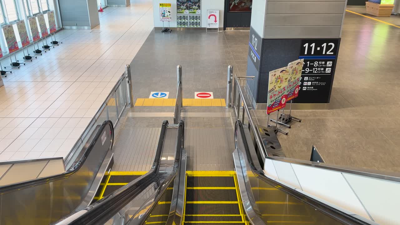 Una ripresa statica dall'alto mostra scale mobili vuote che scendono in un terminal ferroviario pulito e moderno