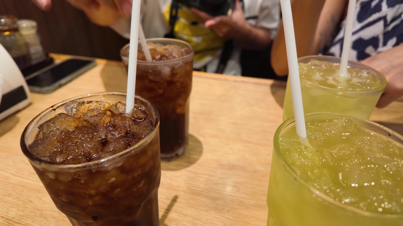 Primer plano de bebidas frías de té helado y refrescos con pajitas en una mesa de madera