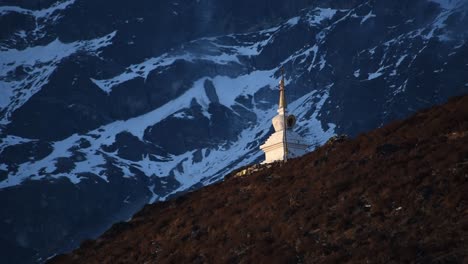 Close-up-view-of-a-sun-lit-white-stupa-in-front-of-a-massif-towering-montain-slope-in-the-Himalayas