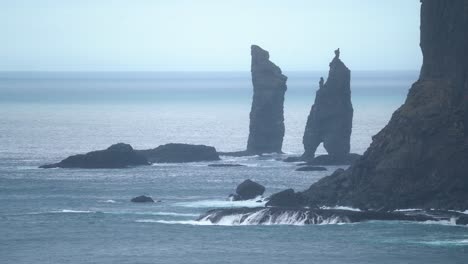 wide shot showing risinn og kerlingin sea stacks on streymoy island with crashing waves - slow motion