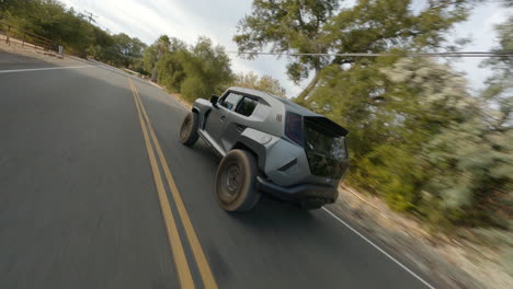 tracking fpv shot of futuristic off road car driving on rural road under blue sky