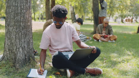 Afrikanischer-Student-Benutzt-Laptop-Und-Macht-Sich-Notizen-Im-Park