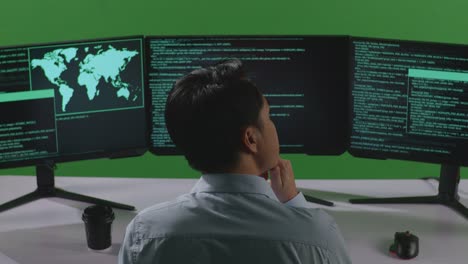 vista trasera de un hombre asiático desarrollador pensando en algo luego levantando su dedo índice mientras escribe código con múltiples pantallas de computadora en el estudio de pantalla verde