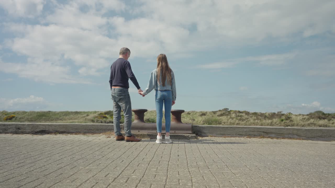 Father and daughter holding hands, chatting and bonding, wide shot