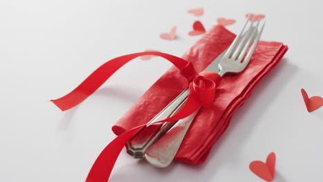 Cutlery-and-red-ribbon-with-paper-hearts-on-pink-background-at-valentine's-day