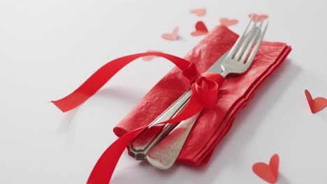 cubiertos y cinta roja con corazones de papel sobre fondo rosa en el día de san valentín