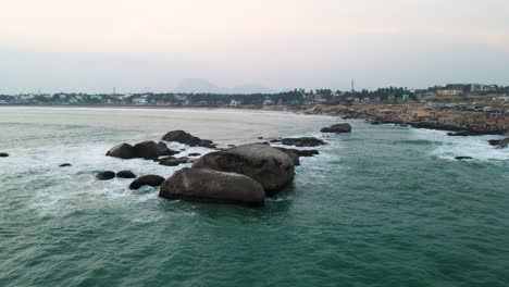 immersive aerial drone shot of kanyakumari's ocean waves lapping the shore as the city unwinds at sunset.