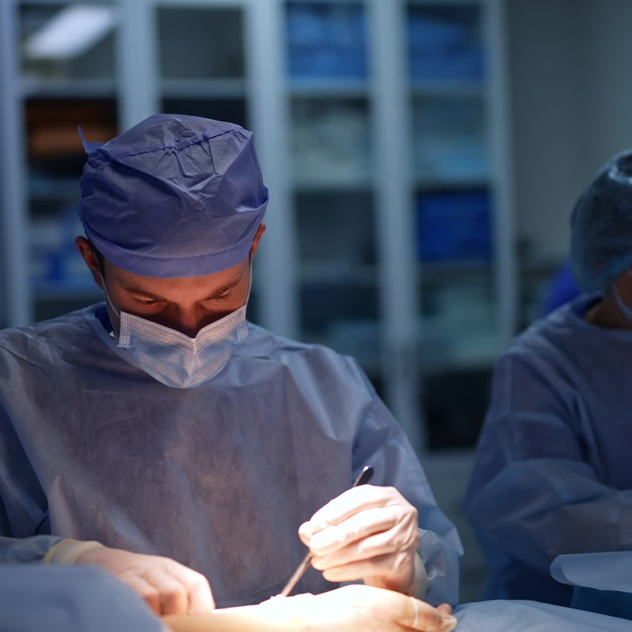 Carefully working surgeon during neurosurgery. Doctor in mask using metal tools as well as modern devices. Female nurse standing behind