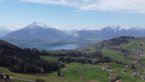 drone flight through a green valley towards a deep blue mountain lake with the swiss alps in the background