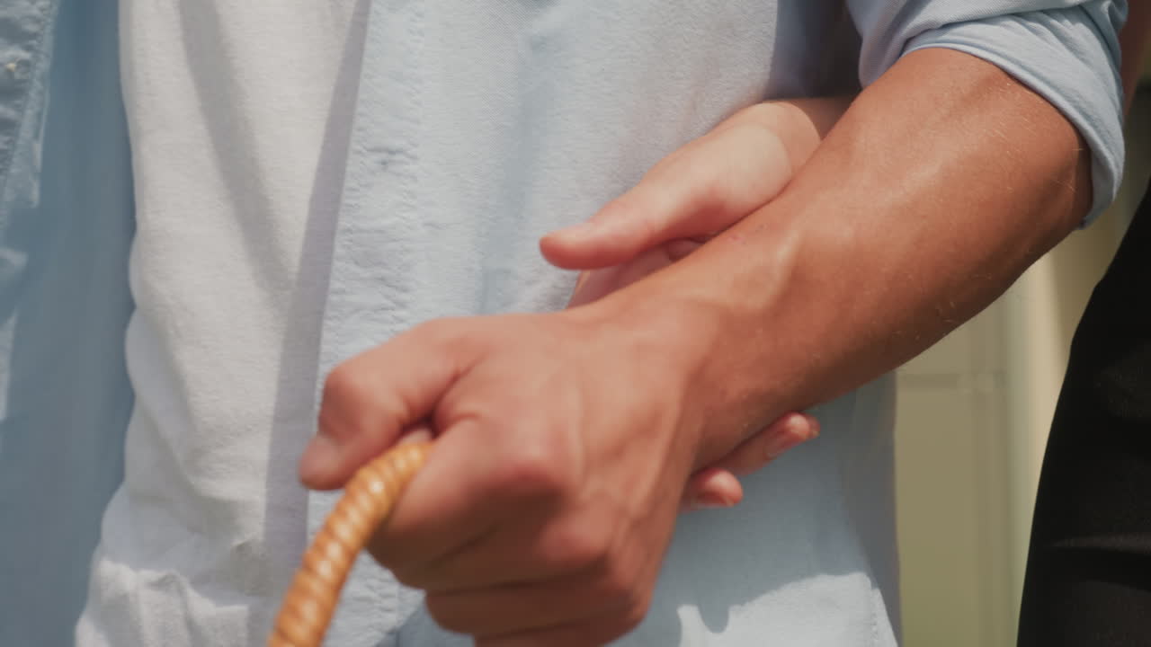 Casal de braços dados ao lado de uma cesta de piquenique, close ensolarado do braço masculino em uma camisa clara e mão feminina no cotovelo, gesto íntimo, roupa casual de verão, conexão calorosa, clima romântico ao ar livre