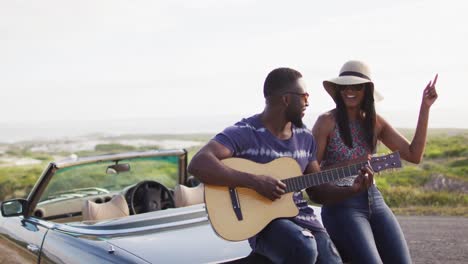 Hombre-Afroamericano-Tocando-La-Guitarra-Para-Su-Novia-Mientras-Está-De-Pie-En-La-Carretera