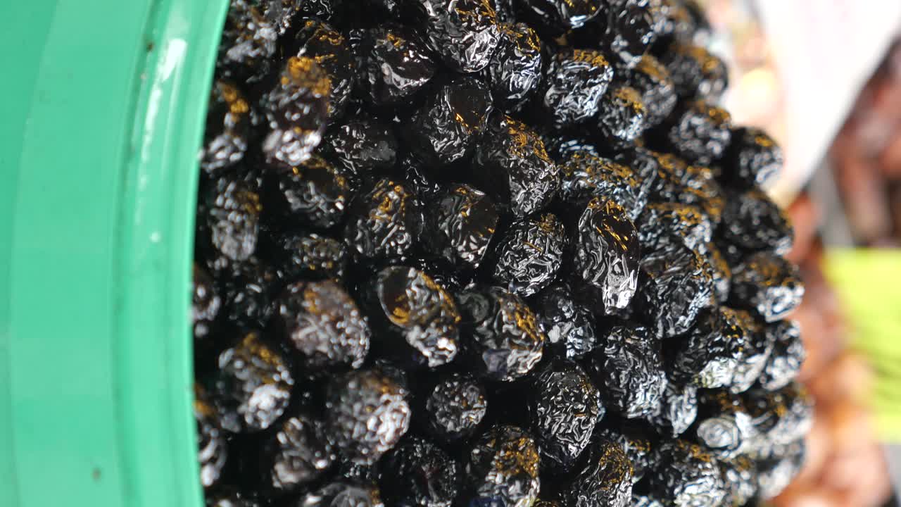 A close-up of black olives or prunes in a green container