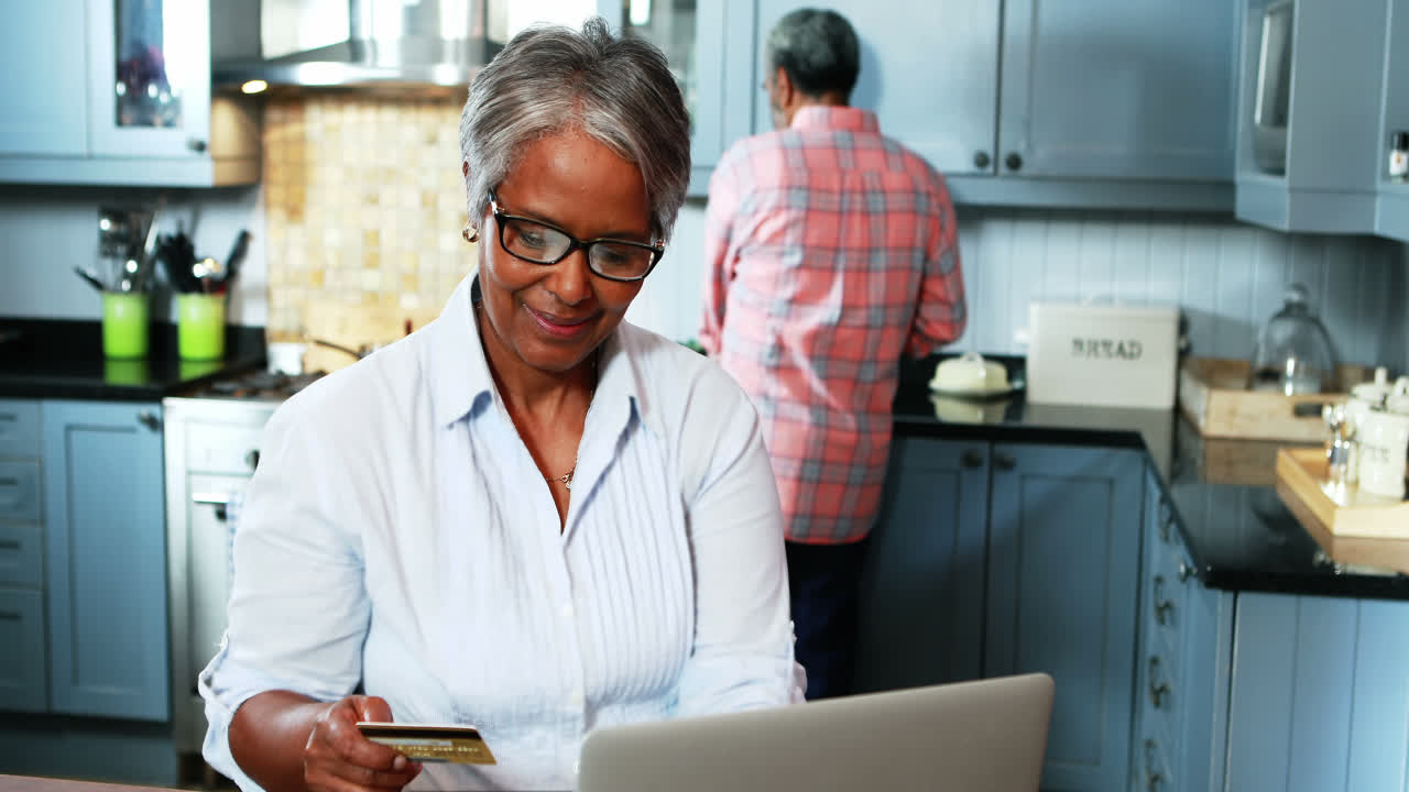 Senior woman doing online shopping on laptop in kitchen at home