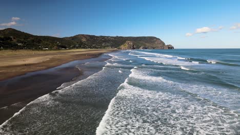 Flying-low-across-shallow-surf-and-black-sand-beach