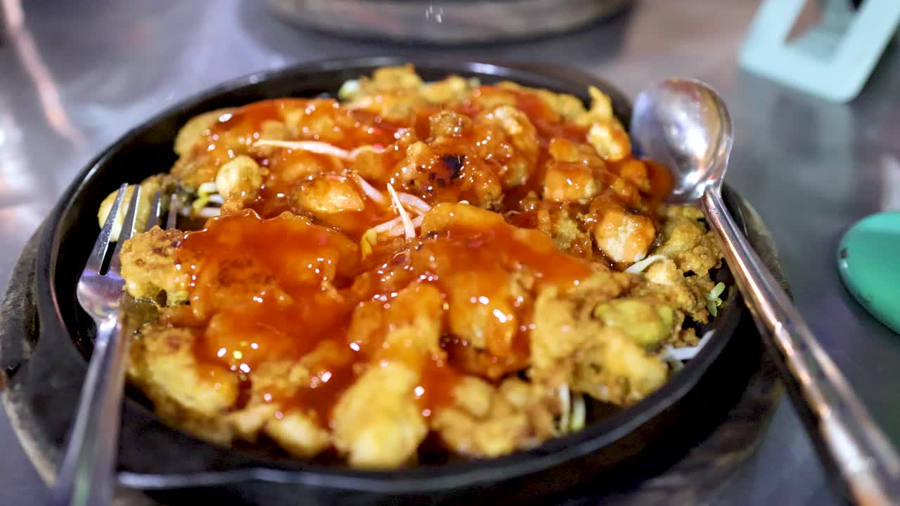 Hot oyster pancake on skillet, sauce poured, garnished at night street food market, overhead view